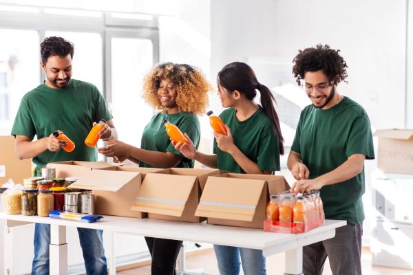charity, donation and volunteering concept - international group of happy smiling volunteers packing food and drinks in boxes at distribution or refugee assistance center